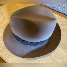 This Classic Turn Down Brim Fedora Is Made From Patented Gentlefelt, One Of The Most Comfortable 100% Wool Felt Formulas Ever Produced. The Wilton Fedora Is So Soft That It Literally Wraps Around Your Head, While Maintaining Its Shape Through Almost Any Mishap, Including Rain, Jostling And Getting Folded Under Heavier Objects. This Was A Gift And Never Worn. Made Of A Fur Blend That's Water Resistant. 100% Wool Gentlefelt. Hand Wash Only. Country Gentleman. Packable, Water Repellent, Grosgrain B Classic Fitted Fedora With Flat Bill, Classic Gray Fedora With Curved Brim, Gray Fitted Wide Brim Fedora, Classic Gray Wide Brim Fedora, Classic Gray Wide Brim Felt Hat, Classic Gray Hat Bands With Flat Brim, Classic Gray Flat Brim Hat Band, Gray Short Brim Hat For Kentucky Derby, Classic Gray Brimmed Hat