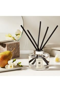 a white table topped with a glass jar filled with candles and a pear next to a mirror