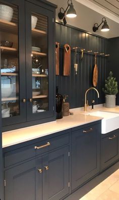 a kitchen with dark blue cabinets and white counter tops, gold faucets and hanging utensils