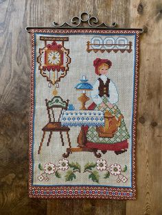 a cross - stitched wall hanging with a woman and child at a tea table