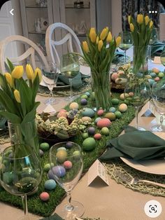 an easter table setting with flowers, eggs and greenery in vases on the table