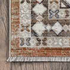 an orange, brown and white rug with fringes on top of wooden flooring