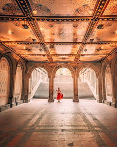 a woman in a red dress is walking through an ornate building with stairs and arches