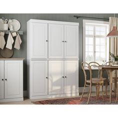 a kitchen with white cupboards and chairs next to a dining room table in front of a window