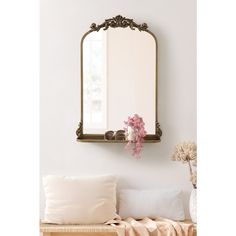 a mirror hanging on the wall above a bench with pillows and flowers in front of it