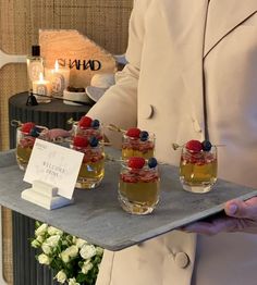 a man in a white suit holding a tray with desserts and drinks on it