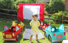 a little boy standing in front of some toy cars on the grass with an italian flag behind him