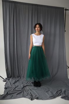 a woman standing in front of a gray backdrop wearing a green tulle skirt and white crop top