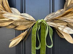 a wreath with gold leaves and green ribbon hanging on the front door to give it a festive touch