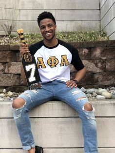 a young man sitting on a ledge holding a skateboard and wearing ripped blue jeans