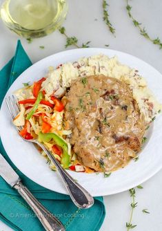 a white plate topped with meat covered in gravy and veggies next to a glass of wine