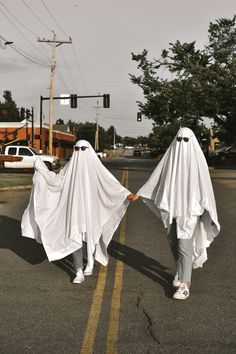 two people in white cloths walking down the street with their arms wrapped around each other