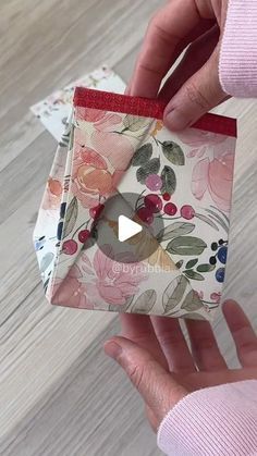 someone is holding an origami box with flowers on it and a red ribbon