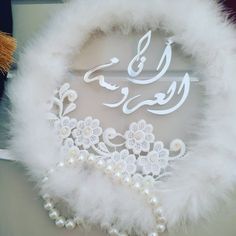 a white feather wreath with an arabic calligraphy in the middle and pearls on it