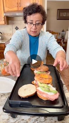 an older woman is making sandwiches on a tray at the kitchen counter, ready to be served