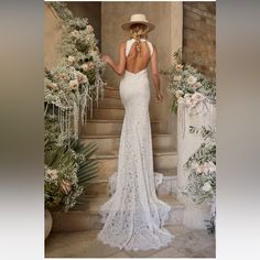 a woman in a white dress and hat walking down stairs with flowers on the steps