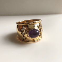 This is a beautiful statement ring. It features a vibrant purple amethyst Cabochon center stone with 6 round brilliant diamonds set in square boxes. The band is a nice thick width of 16.48mm. Amethyst is the birthstone of February. This cabochon cut Amethyst is a beautiful saturated lilac color. 1970s Vintage. Excellent condition. Metal:18k Yellow Gold. Weight: 9.47 grams Diamonds: .20ct size 9 With any pre-owned/Vintage/Antique items, it is common to have some wear, As we inspect each piece of Gold Gemstones Ring With Gemstone Accents, Formal Fine Jewelry Amethyst Ring, Elegant Amethyst Rings With Stones, Gold Spiritual Rings With Gemstone Accents, Spiritual Gold Rings With Gemstone Accents, Heirloom Round Jeweled Jewelry, Elegant Amethyst Crystal Ring With Stone Setting, Purple Jeweled Round Jewelry, Gold Amethyst Oval Cabochon Ring