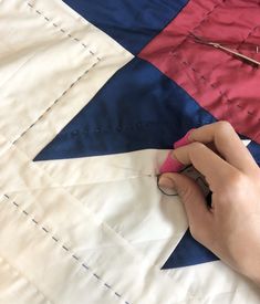 a person cutting fabric with scissors on top of a piece of cloth that has been stitched together