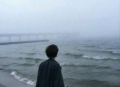 a man standing on top of a beach next to the ocean with a bridge in the background