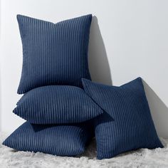 three blue pillows stacked on top of each other in front of a white wall and carpet