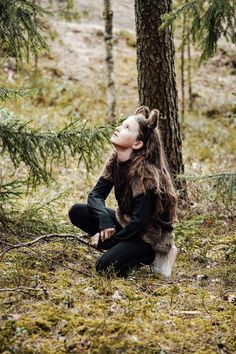 a woman with long hair sitting on the ground next to a tree and looking up