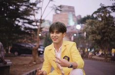 a young man in a yellow suit sitting on the ground with his hands out and smiling