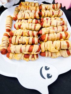 hotdogs wrapped in bacon are on a white platter at a halloween party