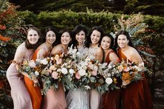 a group of women standing next to each other in front of trees and bushes holding bouquets