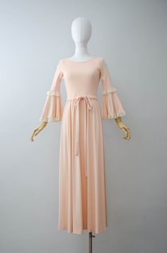 A peach maxi dress with a stretchy ribbed bodice. The half sleeves and skirt are done in a silky polyester with the bell sleeves being trimmed in lace. A drawstring tie is found at the waist and it has a back zip closure. ☛ m e a s u r e m e n t s ☚ Bust: 32-36 Waist: 27-34 Hips: open Shoulders: 11.5-14 Length: 55 ☛ d e t a i l s ☚ Era: 1970s Material: polyester Condition: excellent ☛ v i s i t t h e s h o p ☚ https://etsy.me/2Nd23kg ☛ instagram ┇ poppycockvintage ☛ facebook ┇ poppycockvintage Elegant Summer Maxi Dress With Bell Sleeves, Spring Bell Sleeve Stretch Dresses, Elegant Bell Sleeve Maxi Dress For Summer, Spring Stretch Bell Sleeve Dresses, Spring Beige Stretch Maxi Dress, Beige Stretch Maxi Dress For Spring, Feminine Fitted Peach Maxi Dress, Peach Fitted Floor-length Maxi Dress, Fitted Apricot Maxi Dress For Spring