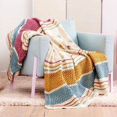 a blue chair with a multicolored blanket on it and a pink wooden table in the background