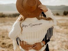 a woman wearing a cowboy hat and white shirt with words on it, standing in an open field