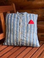 a blue striped shirt with a red heart on it sits on a wooden bench next to a pillow