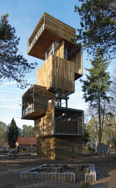 a tall wooden structure sitting on top of a dirt field next to trees and grass