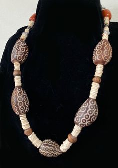 "This bold, festive necklace features large carved nuts with lines of overlapping bullseye circles interspersed with ostrich egg shell heishi beads, wood beads, metal cornerless cubes and disks and reddish amber colored phenolic resin (bakelite) beads with darkened, burnt looking areas. The description sounds a bit weird but I think the necklace is handsome. It is strung on very sturdy nylon cord. The necklace is 26\" long. It has no clasp" Traditional Brown Carved Jewelry, Traditional Brown Oval Beads Jewelry, Bohemian Brown Carved Beaded Necklaces, Bohemian Brown Carved Beaded Necklace, Bohemian Brown Beaded Carved Necklace, Brown Carved Round Beads Necklaces, Brown Carved Round Bead Necklaces, Unique Carved Brown Necklace, Unique Brown Carved Necklace