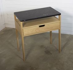 a small wooden table with a drawer on it's side and a white wall in the background