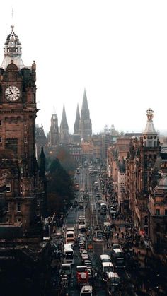 a city street filled with lots of traffic next to tall buildings and clock tower in the distance