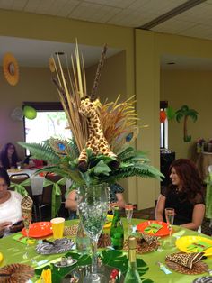 people sitting around a green table with plates and cups on it, in front of a giraffe statue