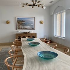 a long table with blue glass bowls on it in front of a painting and chandelier