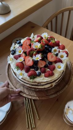 a cake with strawberries, blueberries and daisies on it sitting on top of a wooden table