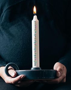 a person holding a plate with a lit candle in it's center and writing on the side