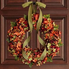 a wreath is hanging on the front door with green ribbon around it and flowers in the middle