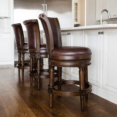 a kitchen with white cabinets and wooden floors, along with brown leather bar stools