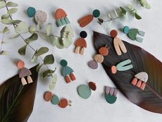 several different shapes and sizes of earrings on a white surface next to a green leaf