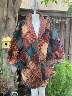 a mannequin wearing a jacket made out of old quilts in front of a tree