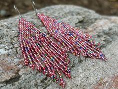 a pair of pink and blue beaded earrings sitting on top of a rock