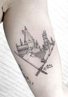 a black and white photo of a castle tattoo on the right arm with writing underneath it