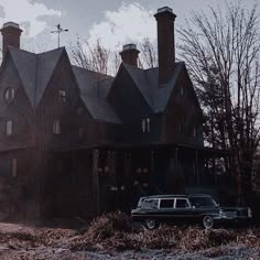 an old black car parked in front of a large house with two chimneys on the roof