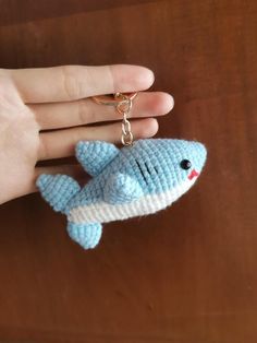 a hand holding a small knitted shark keychain with a chain attached to it