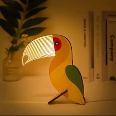 a yellow and green bird lamp sitting on top of a table next to a potted plant