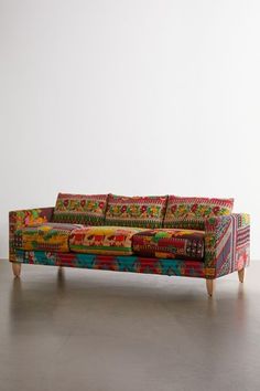 a multicolored couch sitting on top of a hard wood floor next to a white wall